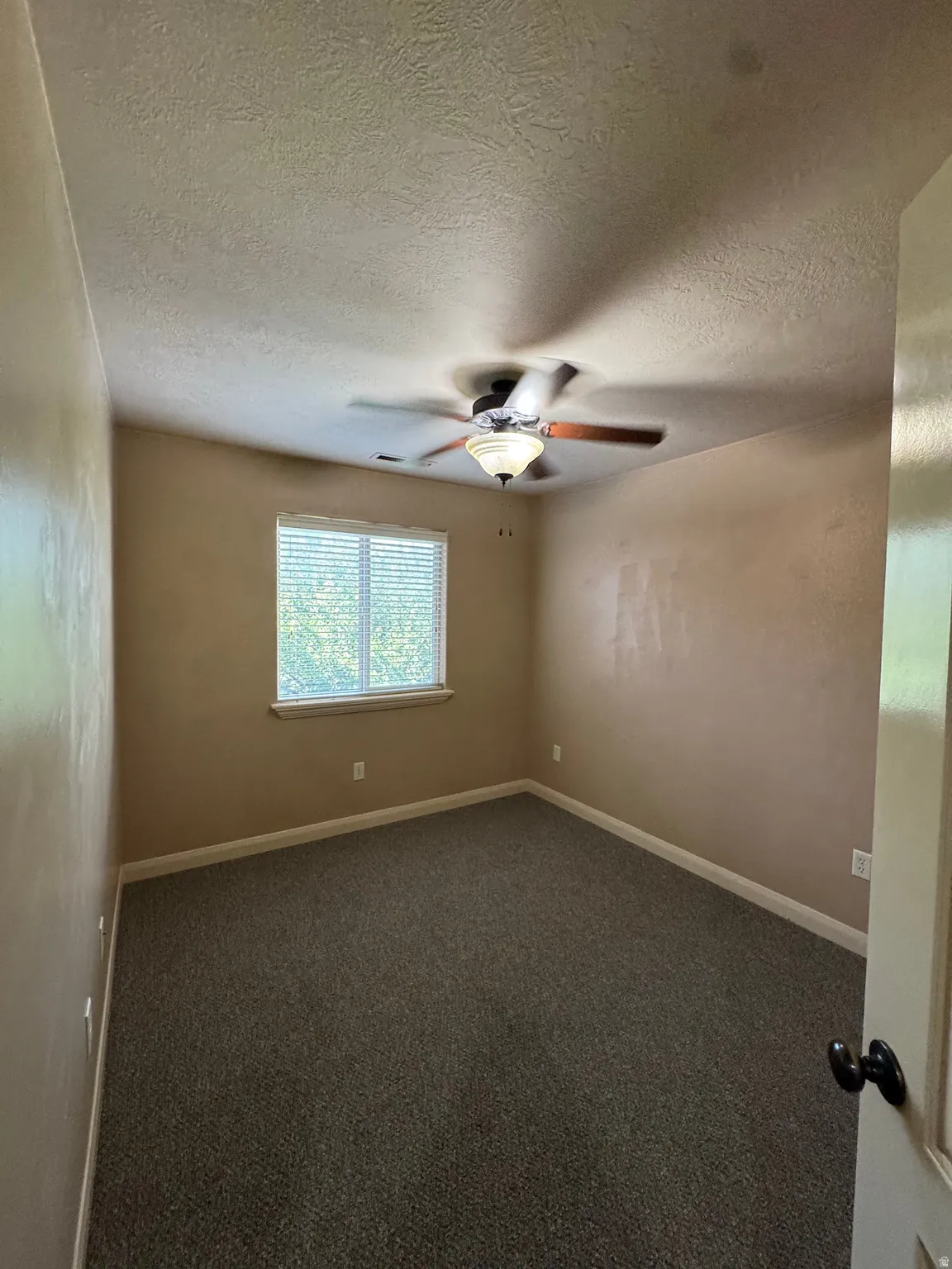 Room with neutral-toned walls, textured ceiling, and a central ceiling fan with integrated lighting