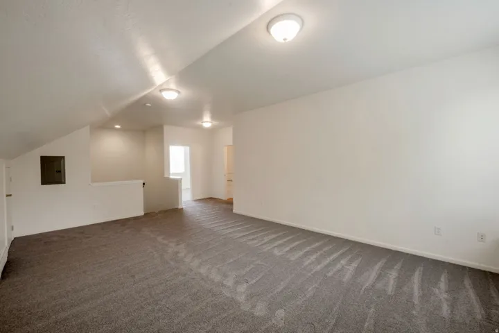 Spacious carpeted room featuring a sloped ceiling, white walls, and flush-mount lighting fixtures