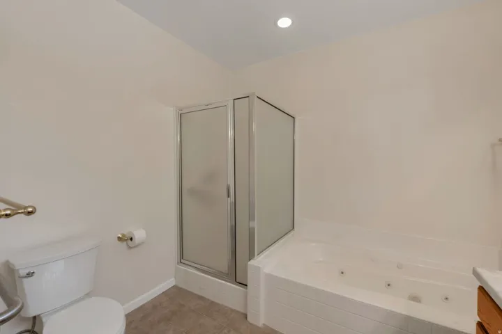Bathroom featuring a corner shower with frosted glass enclosure, a white jetted bathtub, and tile flooring