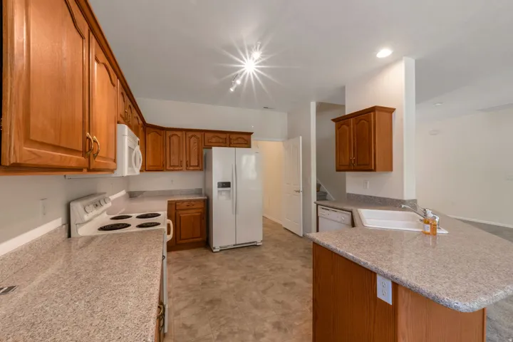 Kitchen featuring wood cabinetry, light-toned countertops, white appliances, and track lighting