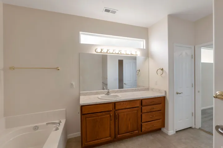 Bathroom featuring a wood-finish vanity with a single sink, an integrated bathtub, and a horizontal transom window