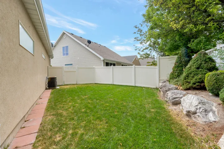 Fenced backyard featuring a manicured lawn, an air conditioning unit, and a landscaped rock garden with established shrubs