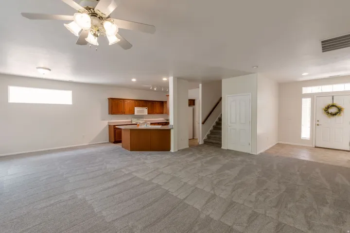 Open concept living space featuring neutral carpet flooring, a ceiling fan with integrated lighting, and a horizontal transom window