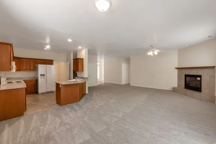 Open-concept living space featuring a fireplace with a stone surround, a ceiling fan, and carpet flooring