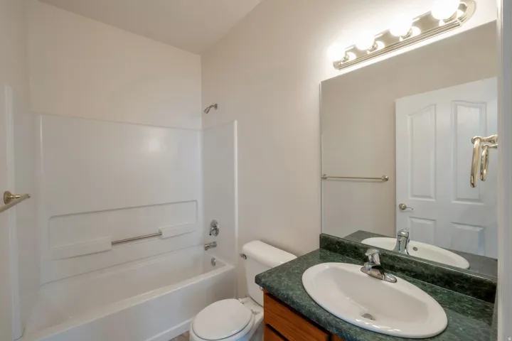 Bathroom featuring a white bathtub with an integrated shower, a vanity with a dark green countertop, an oval undermount sink, and a large wall-mounted mirror