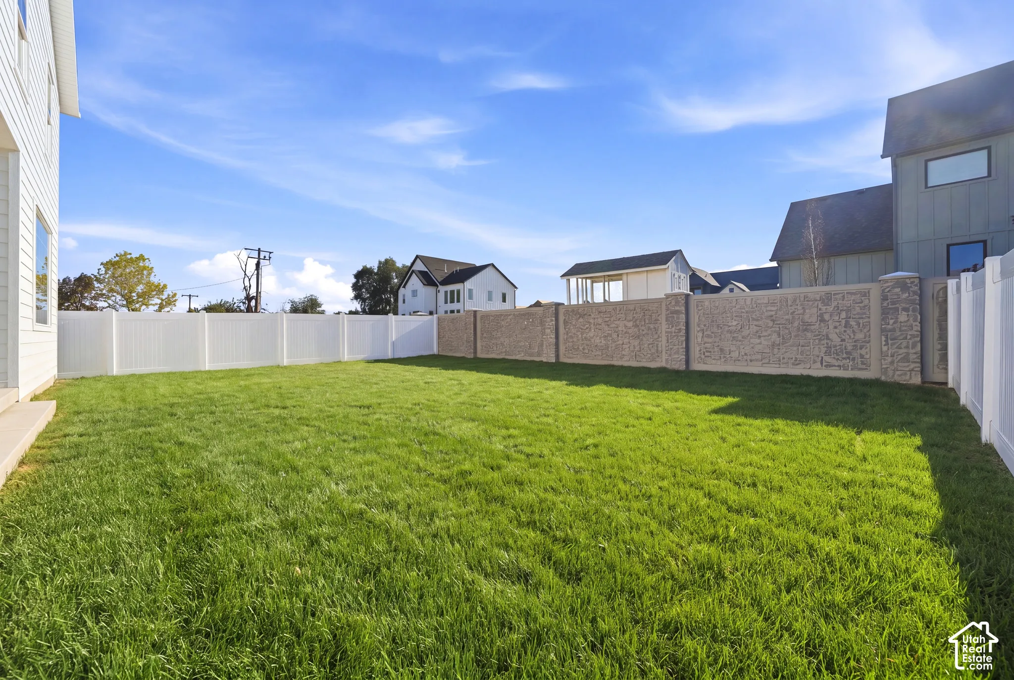 Expansive backyard featuring a lush lawn, white vinyl fencing, and a textured concrete privacy wall *grass ai generated