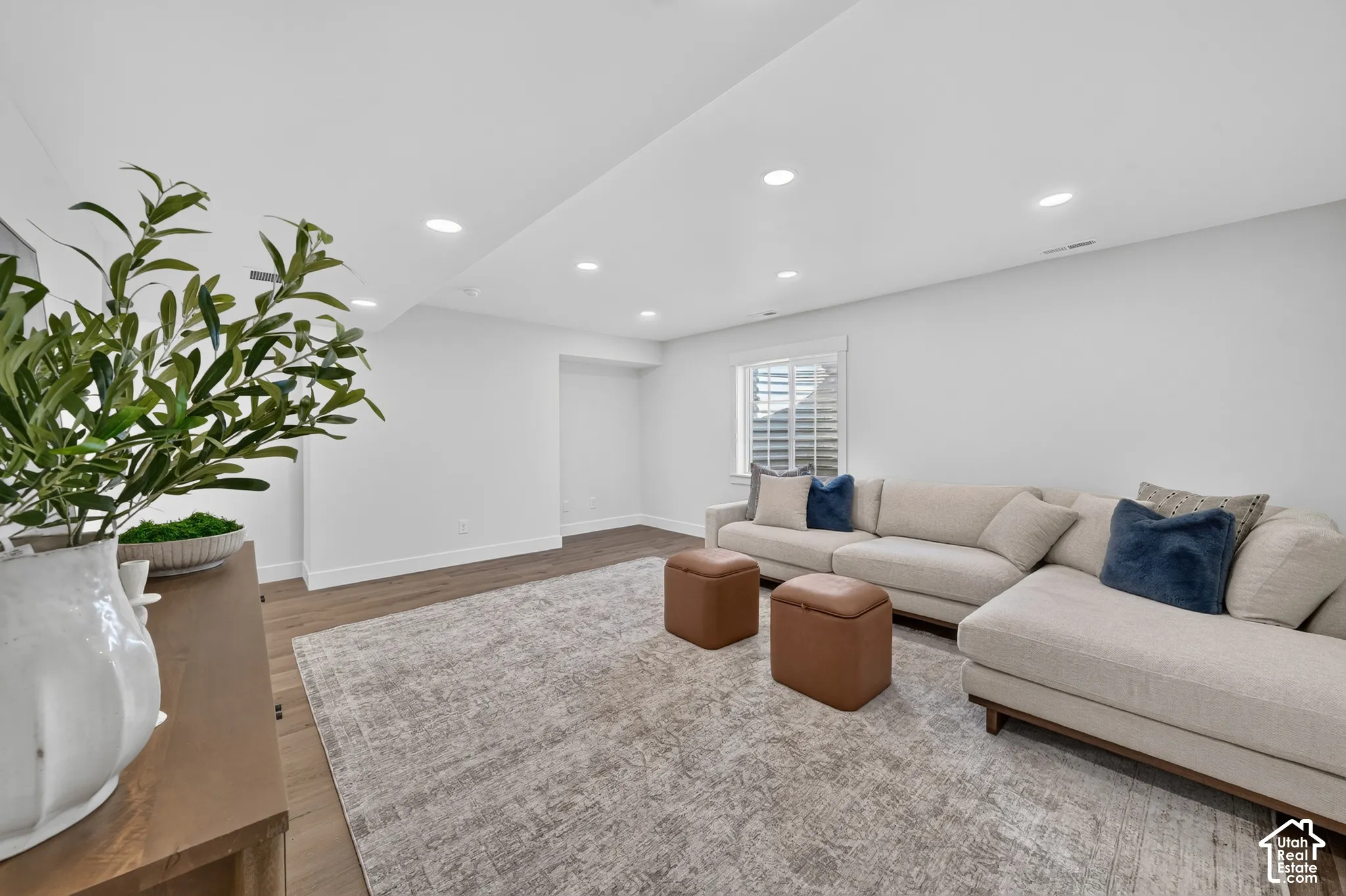 Spacious living area featuring recessed lighting, a window with plantation shutters, wood-finish flooring, and light wall paint
