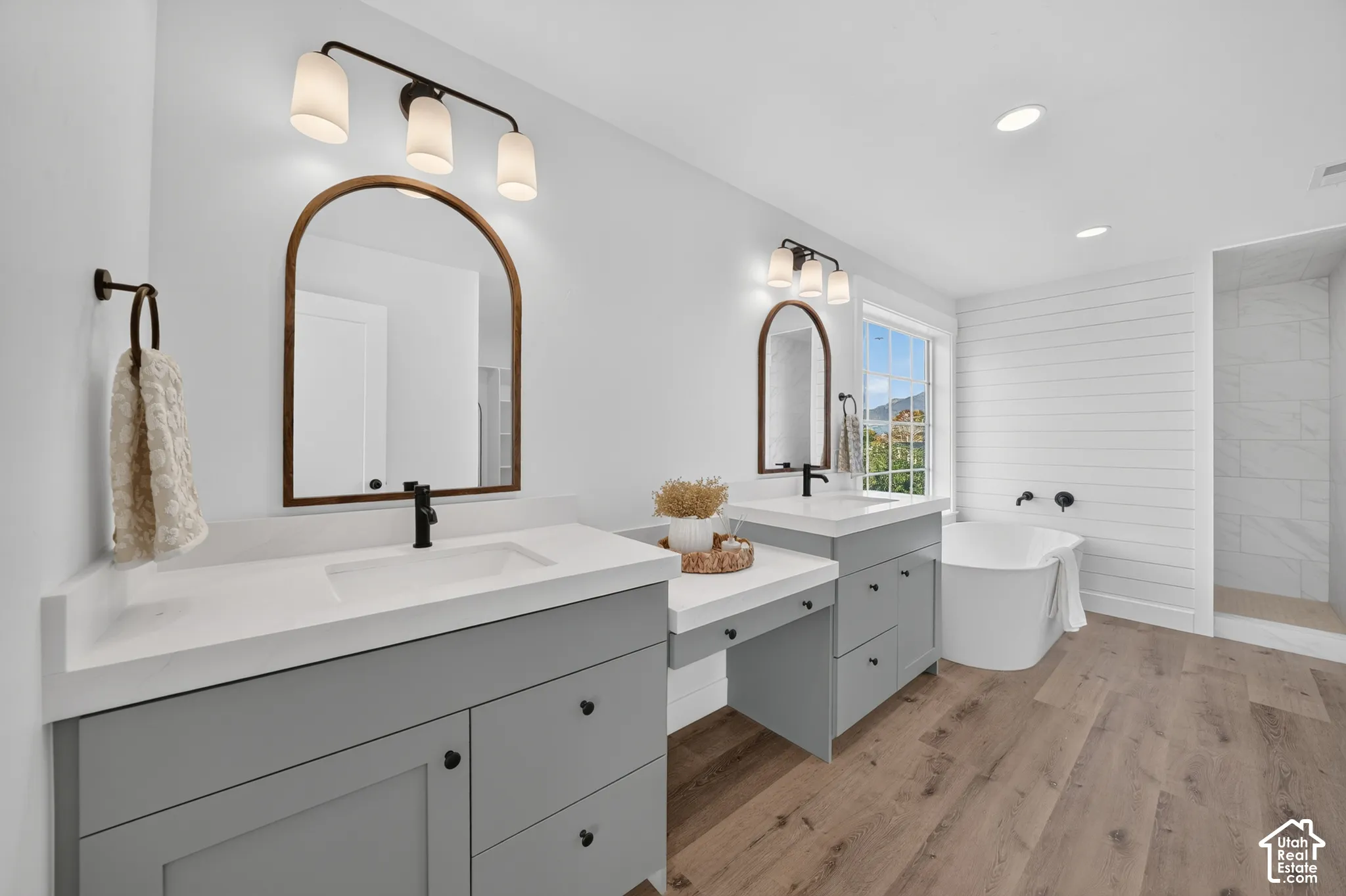 Bathroom featuring dual vanity with gray cabinetry and white countertops, individual arched mirrors, and matte black fixtures