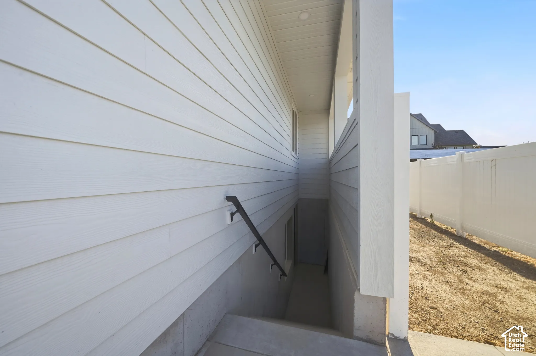 Exterior access featuring white horizontal siding, a black metal handrail, concrete steps, and a white privacy fence