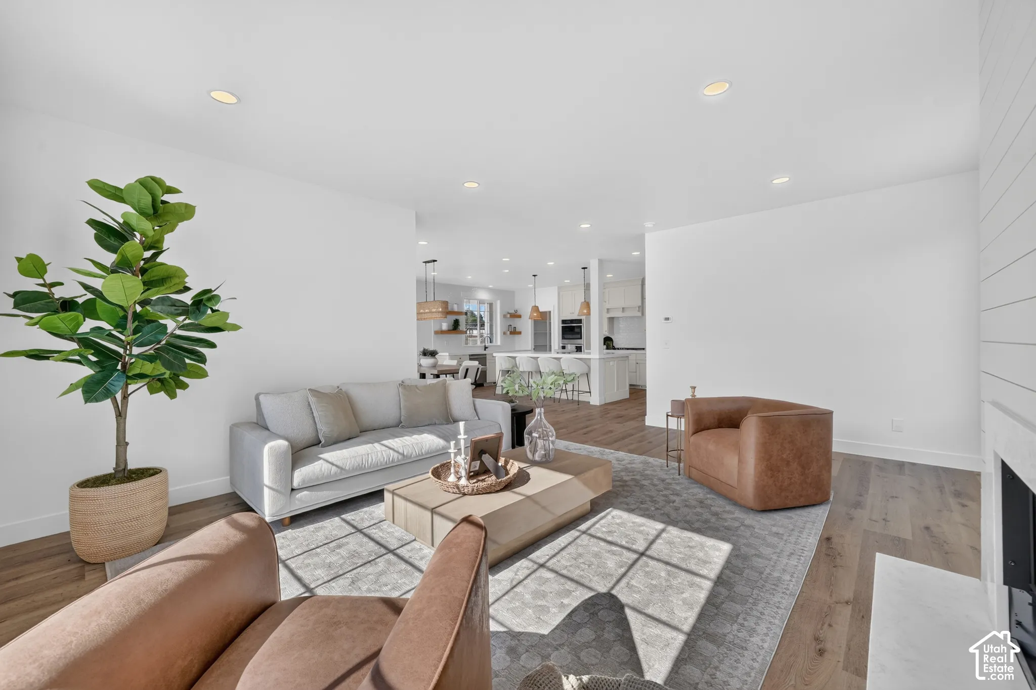 Open-concept living space featuring wood-finish flooring, recessed lighting, and a white shiplap accent wall with a built-in fireplace