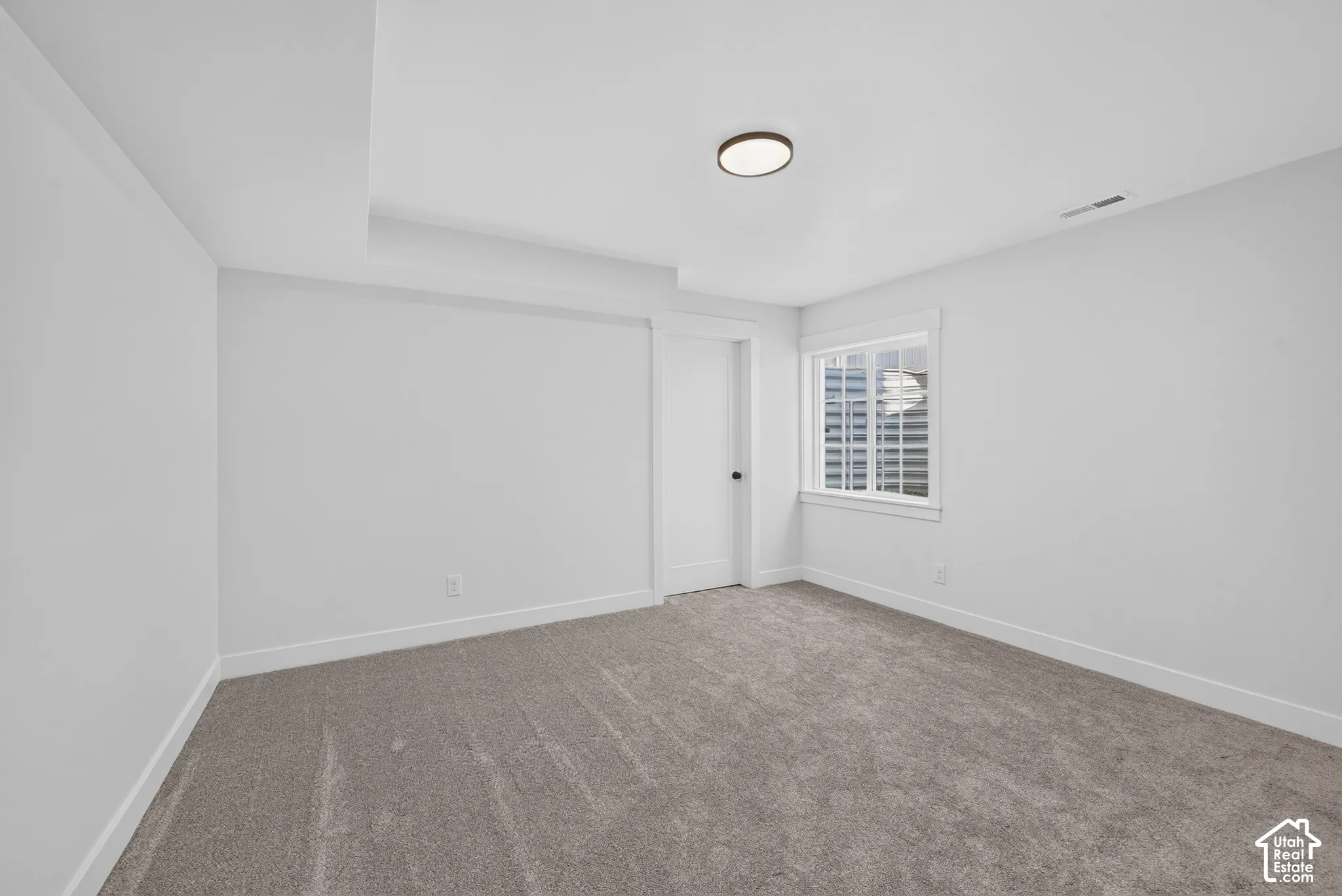 Carpeted room featuring a white door with dark hardware, a window with white louvered blinds, and a ceiling-mounted light fixture