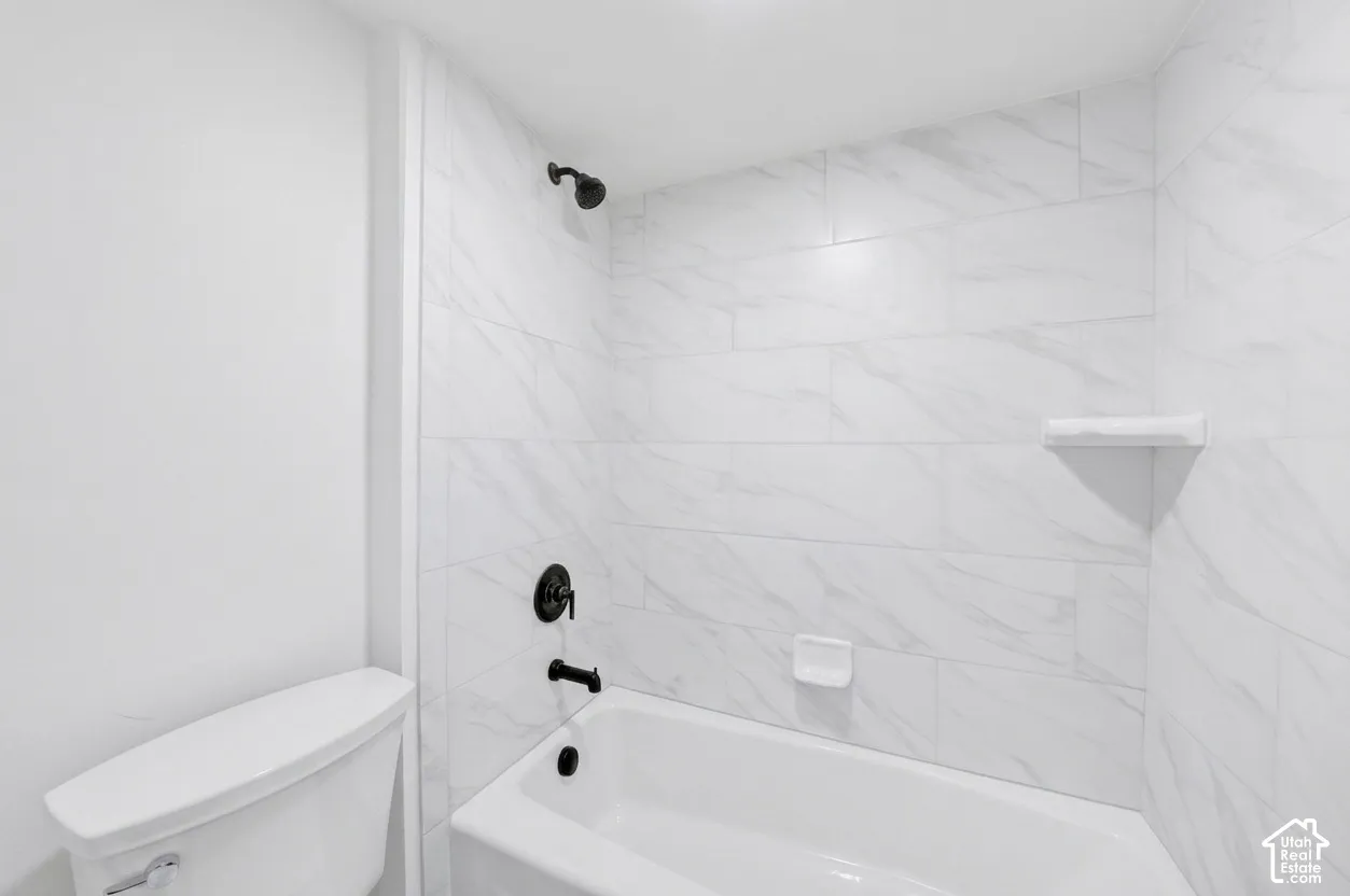 Bathtub shower combination featuring white subway tile surround with subtle veining, matte black fixtures, a built-in soap dish, and a corner shelf