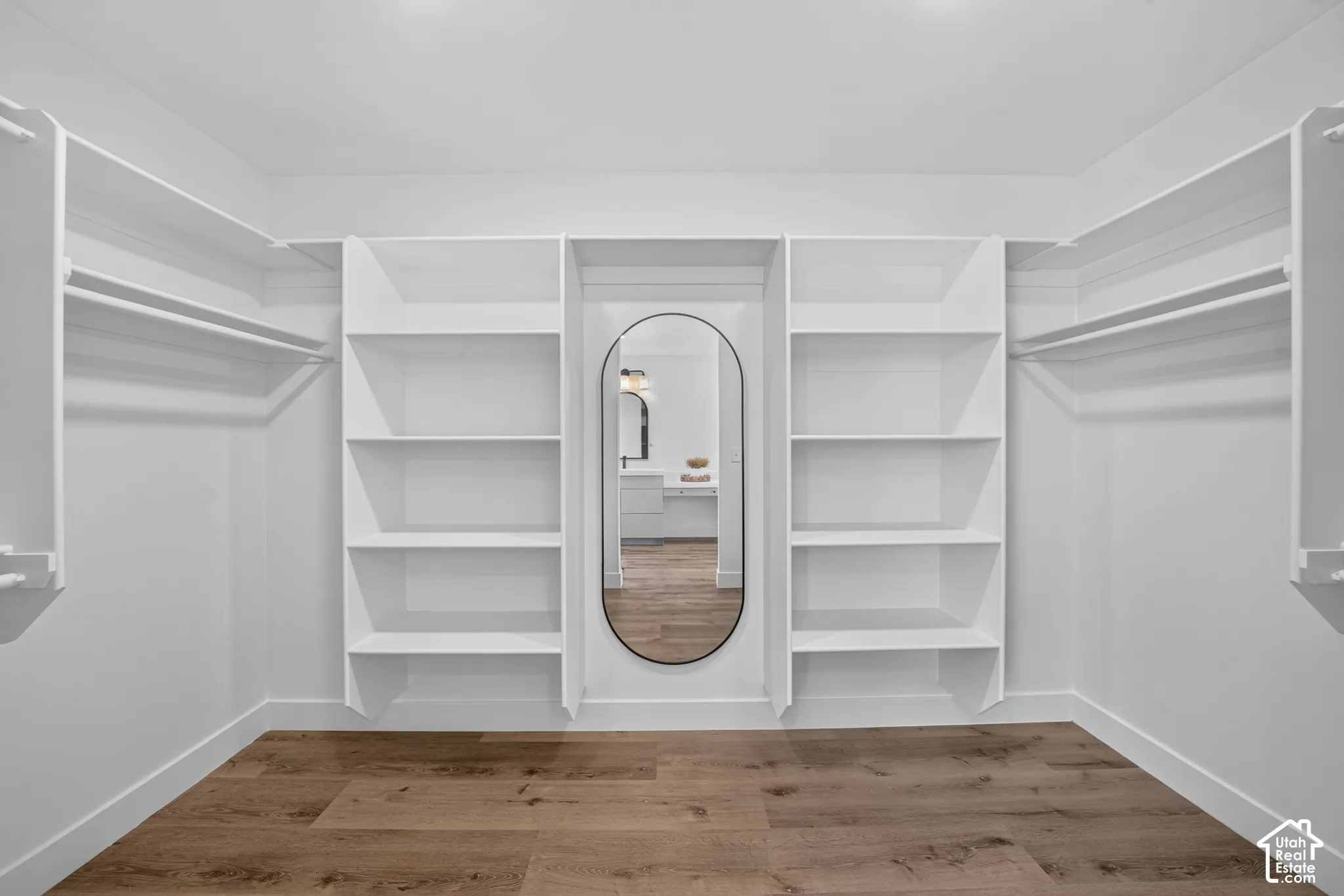 Spacious closet featuring custom built-in shelving, hanging rods, an oval-framed mirror, wood-finish flooring, and crisp white trim