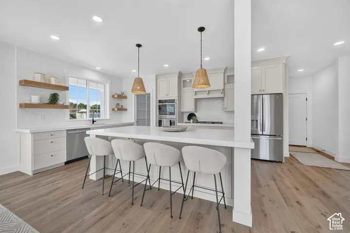 Modern kitchen featuring a large central island with seating, stainless steel appliances, light-toned cabinetry, wood-finish flooring, and recessed lighting