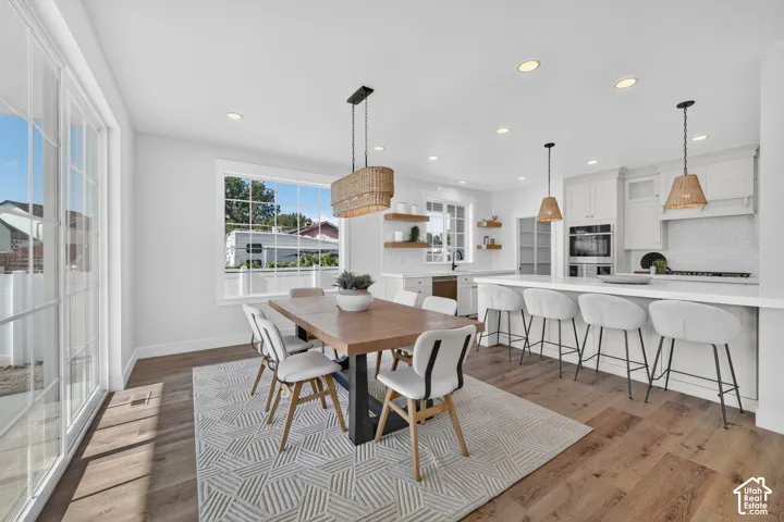 Open-concept dining and kitchen space featuring wood-finish flooring, white cabinetry, a large kitchen island with seating, and sliding glass doors