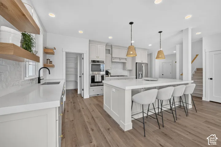 Kitchen featuring a central island with countertop seating, stainless steel appliances, open wood shelving, a tile backsplash, and wood-finish flooring