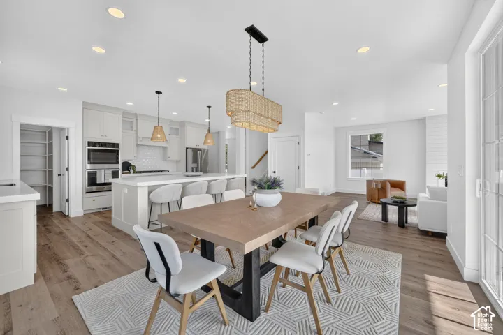 Open-concept living space featuring wood-finish flooring, a contemporary dining area with an overhead woven light fixture, a kitchen island with seating, built-in stainless steel appliances, and a pantry with shelving