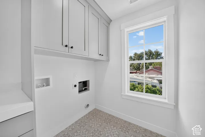 Laundry area featuring patterned tile flooring, shaker-style cabinetry with matte black hardware, and a single pane window with white trim