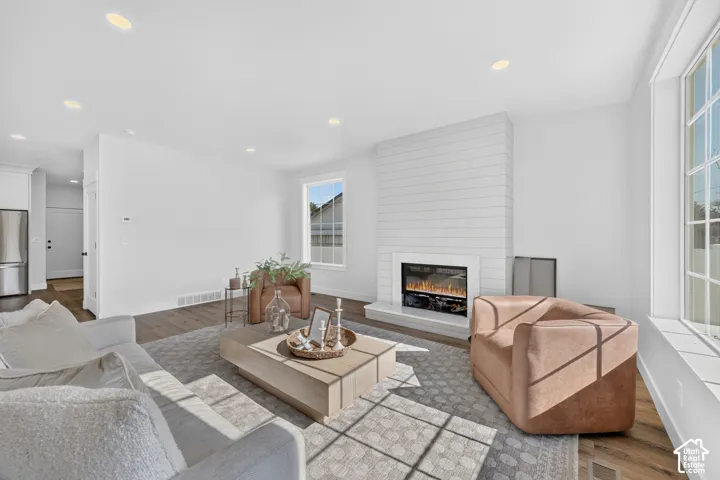 Living space featuring a shiplap fireplace with a white mantel, recessed ceiling lighting, wood-finish flooring, and multi-pane windows