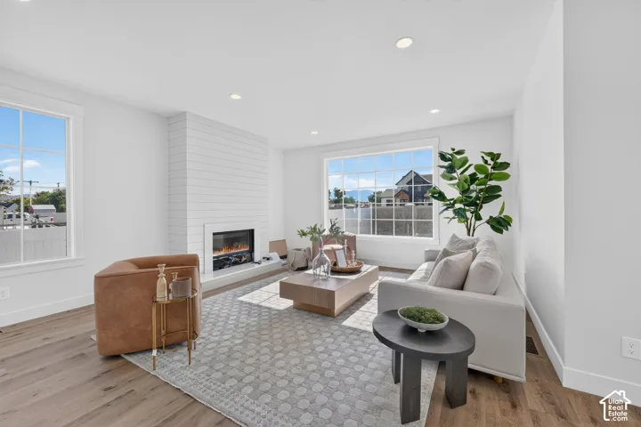 Living area featuring wood-finish flooring, a contemporary fireplace with shiplap-style surround, a large grid-pattern window, and recessed lighting