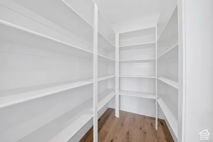 Spacious pantry featuring extensive built-in white shelving, wood-finish flooring, and crisp white baseboards
