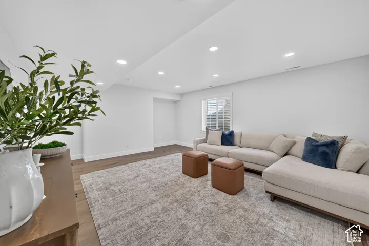 Spacious living area featuring recessed lighting, a window with plantation shutters, wood-finish flooring, and light wall paint