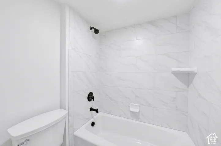 Bathtub shower combination featuring white subway tile surround with subtle veining, matte black fixtures, a built-in soap dish, and a corner shelf