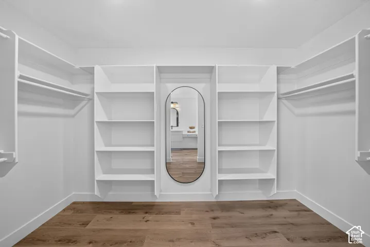 Spacious closet featuring custom built-in shelving, hanging rods, an oval-framed mirror, wood-finish flooring, and crisp white trim