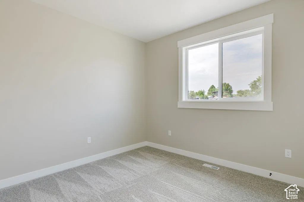 Well-lit room featuring a large window with white trim, light neutral wall paint, and patterned gray carpeting