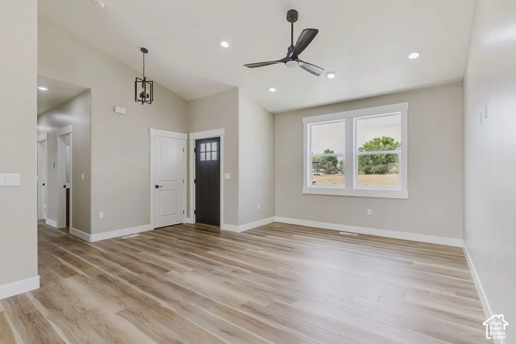 Open-concept living space with vaulted ceilings, recessed lighting, wood-finish flooring, a contemporary ceiling fan, and a black paneled entry door with frosted glass inserts