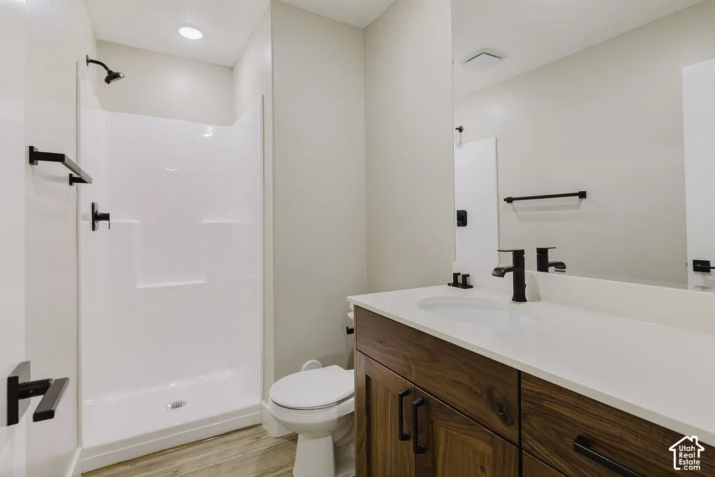Bathroom featuring a white shower stall, wood-finish vanity with an integrated sink, white countertop, and matte black fixtures
