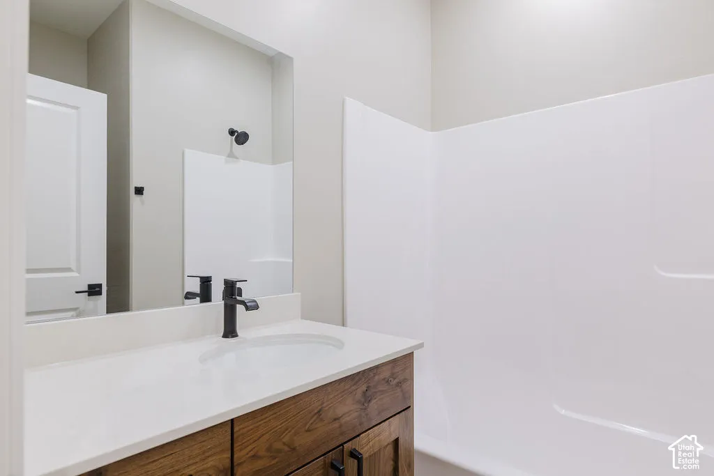 Bathroom featuring a wood-finish vanity with a white countertop and integrated sink, matte black faucet, and a large wall-mounted mirror