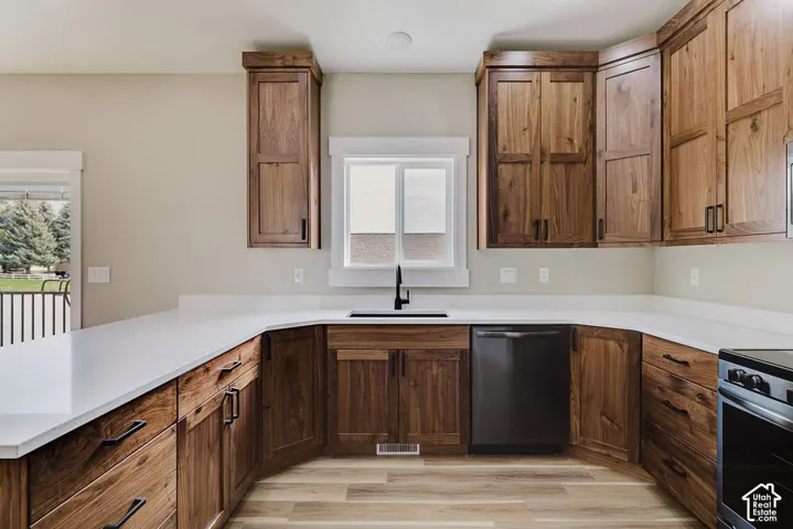 Kitchen featuring wood-finish cabinetry, white countertops, a stainless steel dishwasher, and a black sink with a matte black faucet