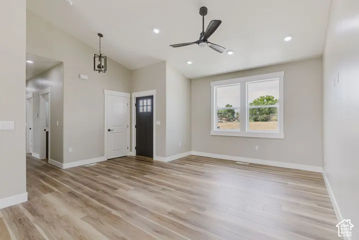 Open-concept living space with vaulted ceilings, recessed lighting, wood-finish flooring, a contemporary ceiling fan, and a black paneled entry door with frosted glass inserts