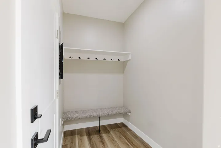 Entryway from garage to mud room with wood-finish flooring, a built-in bench with carpeted top, and a white built-in shelf with black coat hooks