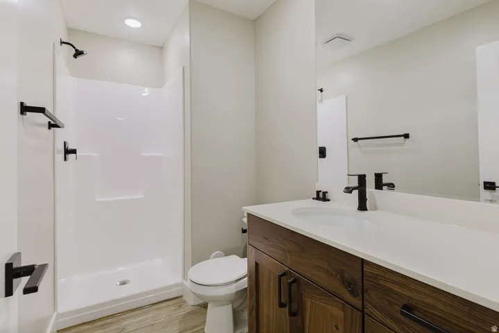 Bathroom featuring a white shower stall, wood-finish vanity with an integrated sink, white countertop, and matte black fixtures