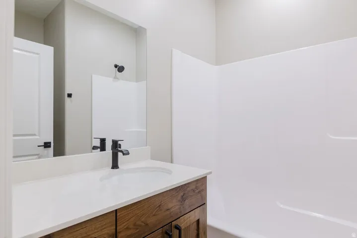 Bathroom featuring a wood-finish vanity with a white countertop and integrated sink, matte black faucet, and a large wall-mounted mirror