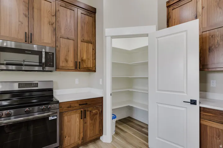Kitchen featuring wood cabinetry, stainless steel appliances, white countertops, and a walk-in pantry with extensive shelving