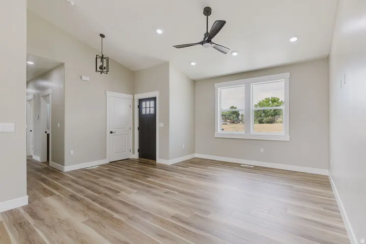 Open-concept living space with vaulted ceilings, recessed lighting, wood-finish flooring, a contemporary ceiling fan, and a black paneled entry door with frosted glass inserts