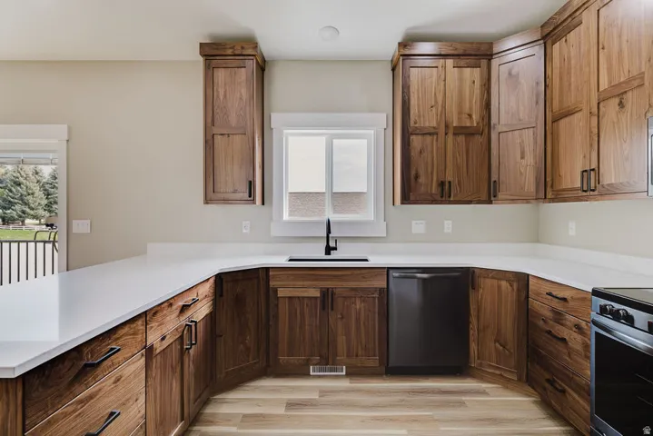 Kitchen featuring wood-finish cabinetry, white countertops, a stainless steel dishwasher, and a black sink with a matte black faucet