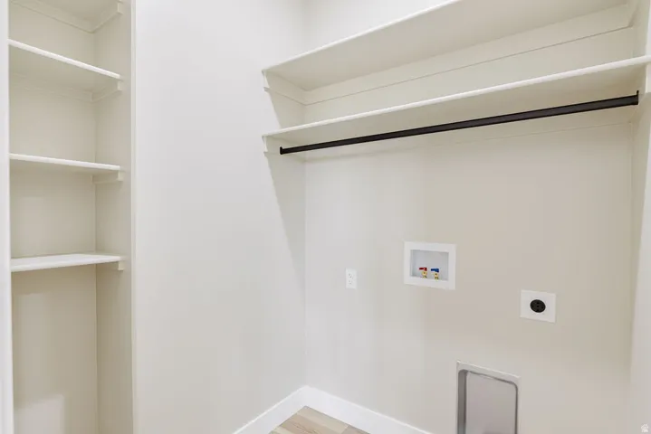 Dedicated laundry space featuring a clothes hanging rod, built-in shelving, washer hookups, dryer vent, and wood-finish flooring