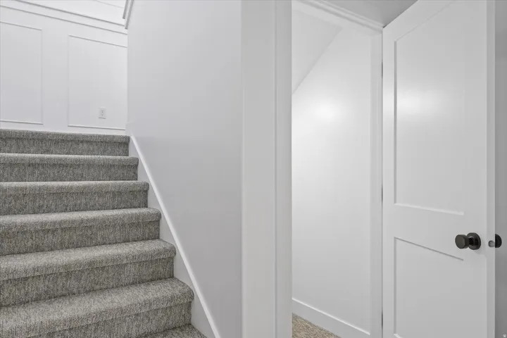 Carpeted staircase with white risers and wainscoting