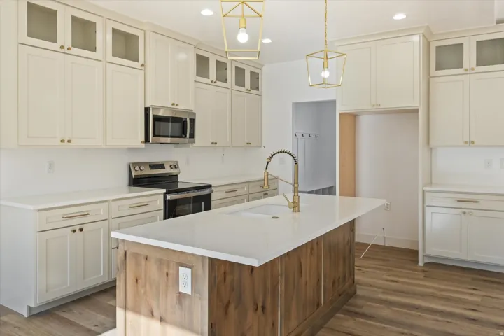 Contemporary kitchen featuring white cabinetry, a wood-finish island with a white countertop, stainless steel appliances, and brass-finish hardware and light fixtures