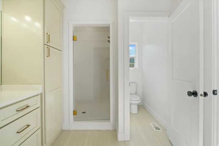 Contemporary bathroom featuring light-toned cabinetry with gold-toned hardware, a glass-enclosed shower with matching gold-toned fixtures, and light wood-finish flooring