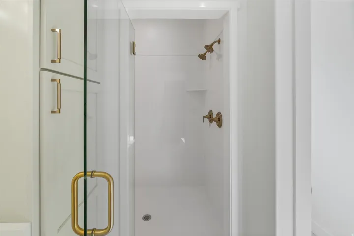 Enclosed shower with clear glass door, gold-finish hardware, and built-in shelving