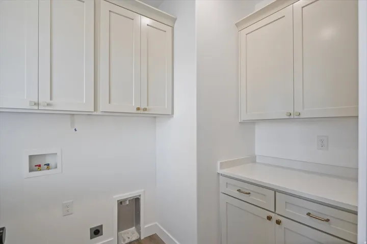 Dedicated laundry space featuring bright white cabinetry with gold-tone hardware, a light countertop, and wood-finish flooring