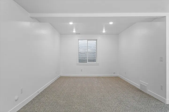 Interior room featuring light-colored carpet, white walls, and a window with a window well