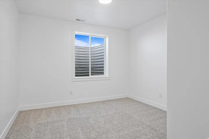 Bright interior room featuring a window with a white frame, light-toned carpeting, white walls, white baseboards, and a ceiling light fixture