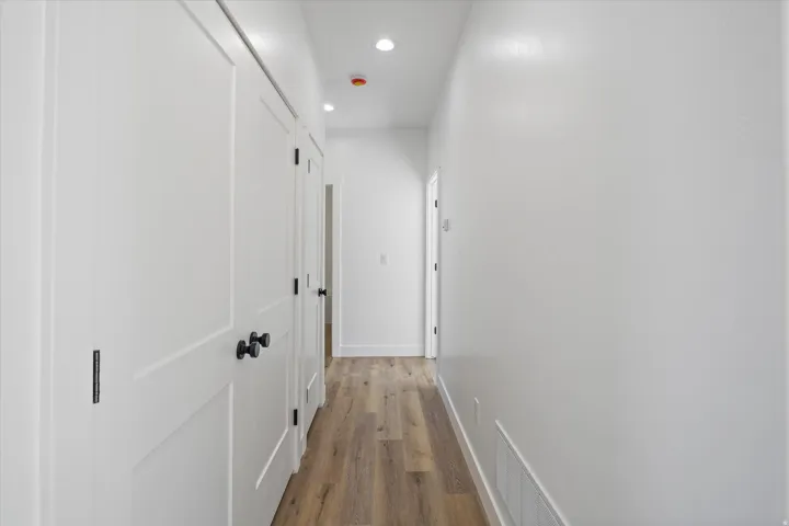 Hallway featuring wood-finish flooring, recessed lighting, white walls, and multiple panel doors with matte black hardware