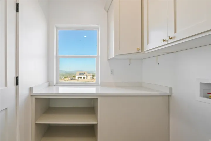 White shaker-style cabinetry with gold-tone hardware, white countertop, built-in shelving, and a dual-pane window